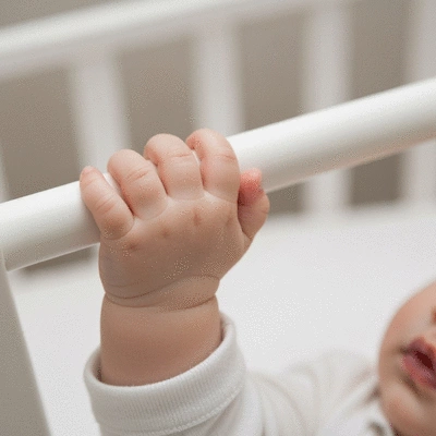 Close-up of a baby's hand gripping a cot bar, illustrating proper bar spacing for safety