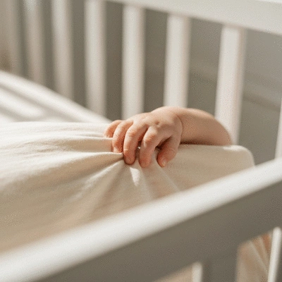 Close-up of a baby's hand clutching a soft, breathable cot sheet in a safe, minimalist cot, no text, no words, no typography, clean image